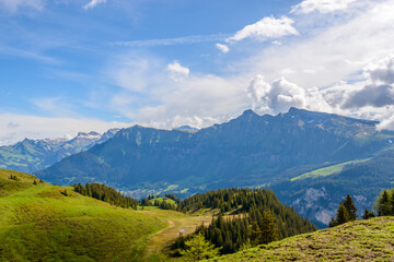 View of beautiful landscape in the Alps with fresh green meadows and snow-capped mountain tops in the background on a sunny day with blue sky and clouds in springtime.