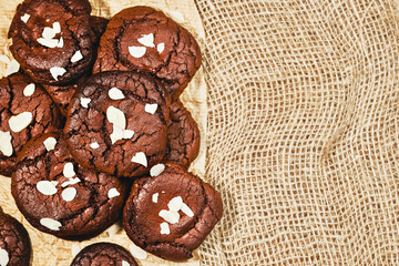 Chocolate freshly baked cookies sprinkled with almond flakes, mock up on paper notebook and burlap background. Top view of cookies with copy space, image for banner or advertisement