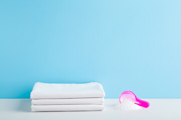 Stack of white bed sheets and cup or scoop of powder on table at light blue wall background....