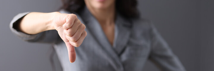 Businesswoman in gray suit holds her thumb down.