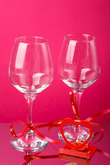 Two champagne glasses with ribbons on a pink background and a heart-shaped candlestick with a candle.