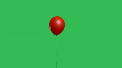Red oval shaped balloon hanging in the air against the background of a green screen chroma key. Colorful helium balloon. Birthday, party decoration, holiday, surprise, gift. Slow motion.