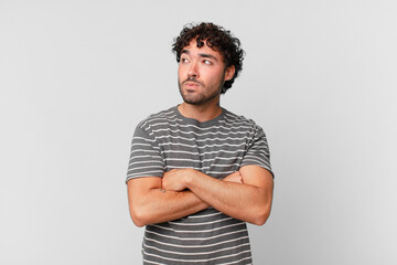 hispanic handsome man shrugging, feeling confused and uncertain, doubting with arms crossed and...