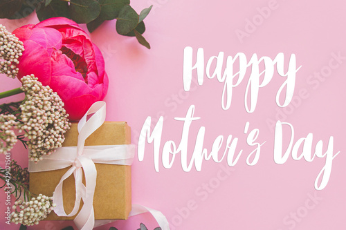 Happy mother's day. Happy mother's day text and modern peony bouquet, gift box with ribbon on bright pink paper flat lay. Stylish floral greeting card. Handwritten lettering. Mothers day