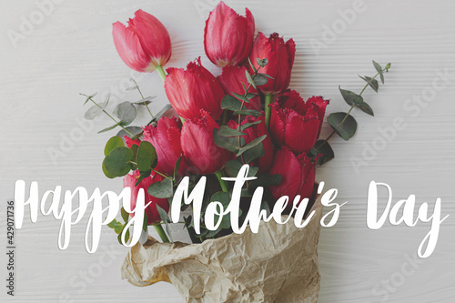 Happy mother's day. Happy mother's day text and red tulips bouquet in craft paper on rustic white wood top view. Stylish floral greeting card. Handwritten lettering. Mothers day