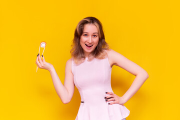 A young caucasian pretty happy  excited smiling brown-haired woman in a light pink blouse advertises sushi holding in bamboo sticks roll philadelphia isolated on a bright color yellow background