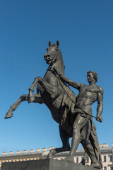 Fototapeta na wymiar Bronze sculpture of athlete taming horse at an Anichkov bridge in St. Petersburg against the blue sky.