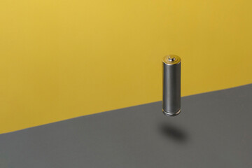 Flying alkaline rechargeable battery against grey and yellow background. Minimal electronic concept.