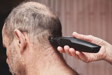 Wife cutting husbands hair at home with a haircut machine or hair clipper.