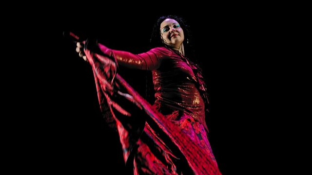 beautiful gypsy woman with long black hair in a red lush dress dances on a black background.