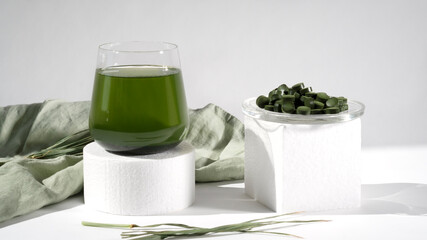 Healthy spirulina drink in the glass with spirulina chlorella pills on podium or pedestal. Modern style. Superfood, detox drink. Healthy care concept.