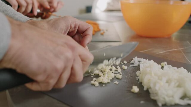 Slow-motion close up of unrecognizable male hands chopping garlic and onion on board during cooking class