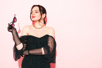 High fashion portrait of young beautiful brunette woman wearing nice trendy summer polka-dot dress and gloves.Sexy fashion model posing near light pink wall in studio.Fashionable female in sunglasses
