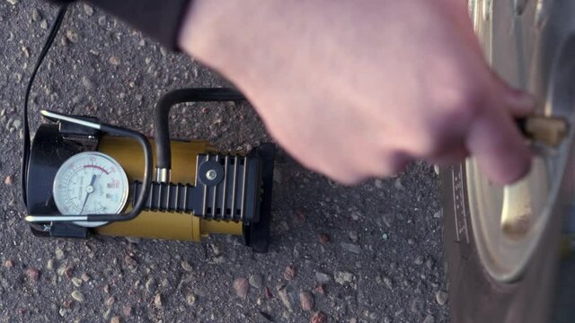 A man tries to pump up a wheel of a car, in focus the pump and a monometer, the concept of a broken car on the road.