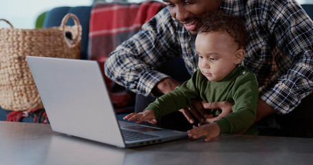 Fototapeta na wymiar Afro-american young dad helping son teaching to use computer laptop sitting in living room playing together. Families. Kids and parents.