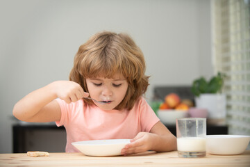 Fototapeta na wymiar Portrait of child eating soup meal or breakfast having lunch by the table at home with spoon. Kids healthy food.
