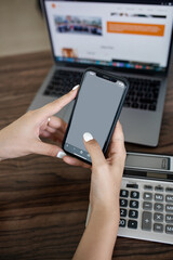 smartphone in women's hands with a white screen in the background of a laptop