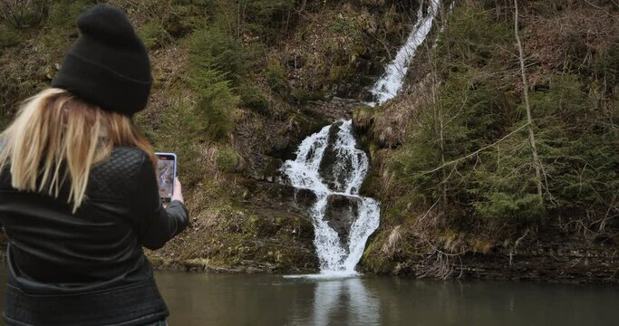Girl tourist is photographed against the background of a waterfall in the Carpathians