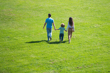 Back view of mother father and child son having fun outdoors at summer park.