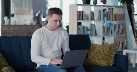 Indoor portrait of attractive young adult using modern mobile laptop computer smiling to camera inside living room. Apartment. Business person.