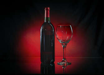 low key image with red light behind wine bottle and red wine glass on reflective surface. 