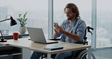 Young attractive adult disabled in wheelchair sitting in corporayte office of contemporary company business center using mobile phone.