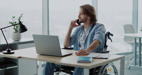 Young handsome office employer boss in wheelchair talking business partner conversation dialing smartphone in corporate office.
