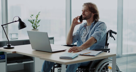 Handsome young invalid disabled man business guy talking on mobile phone in contemporary office....