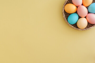 Stylish Easter composition with colorful Easter eggs in pastel colors in a wicker basket on a yellow background with copy space. Top view, flat lay