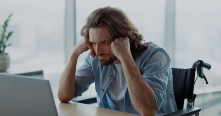 Young depressed office worker sitting by desk worry about work. Disabled invalid young man frutrating having problems at work.