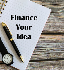 Top view of a pen and a watch with Finance Your Idea written on a notebook.