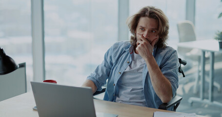 Frustrated young hesitating man using computer laptop sitting by desk doubting what to do....
