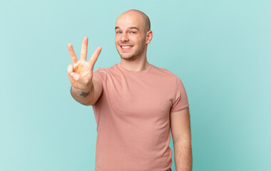 bald man smiling and looking friendly, showing number three or third with hand forward, counting...
