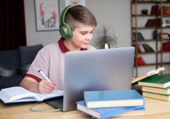 Fototapeta na wymiar teenager boy in headphones studying online using laptop writing in notebook, reading book