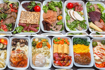 Airplane food presentation with variety of in flight meals.  Flight catering.  Food on airplanes. Salad bar buffet  display in restaurant.  Meat cuts. Hot appetizers. Close-up, a lot of food.
