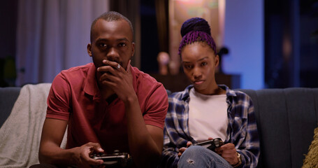 African american love couple at home. Excited male using console gamepad playing online virtual game while his girlfriend using mobile phone.