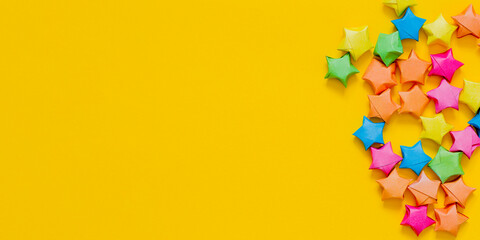 Colorful folded paper stars or origami lucky star on yellow background. Free space for text. Holiday or birthday concept.