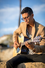 Portrait of Latin man sitting and playing guitar on the street during sunset