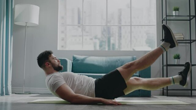 Active bearded athlete guy in t-shirt and shorts trains abs