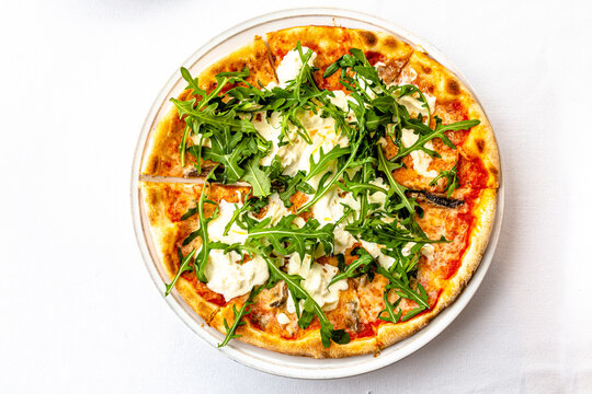 Pizza with arugula and burata is on a plate in a restaurant.