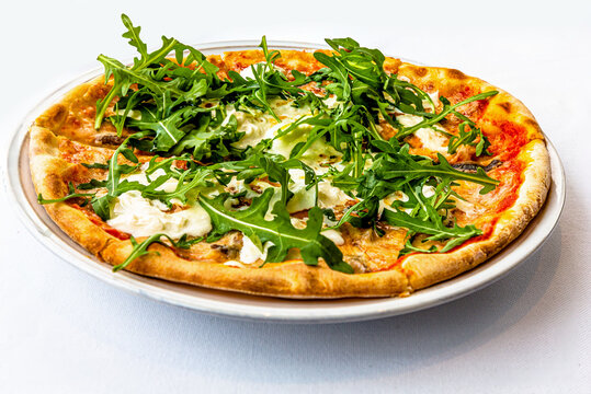 Pizza with arugula and burata is on a plate in a restaurant.