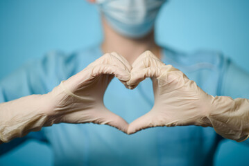 Young woman in medical gloves and protective mask making heart with hands