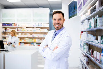 Portrait of smiling caucasian pharmacist standing in drug store with arms crossed.