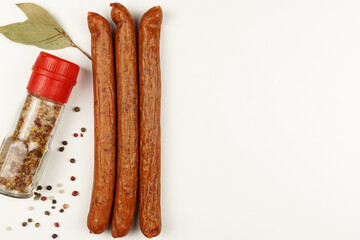 Three sausages are laid out on a white background, next to spices and bay leaf