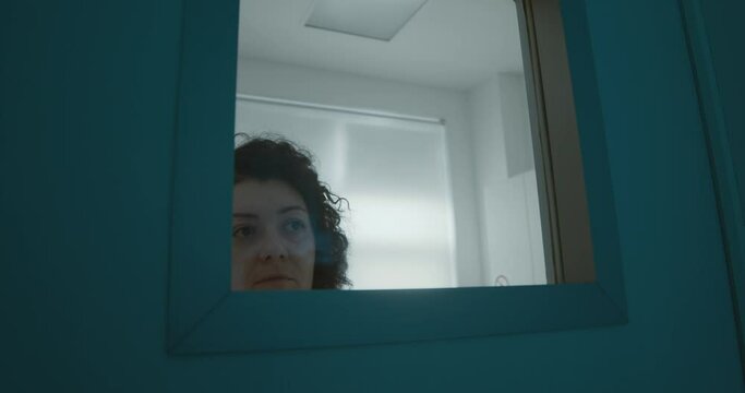 The female medical worker is waiting outside of the dental room and looking at somebody at the window.