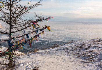 Colored ritual ribbons tied on the tree and wooden poles as a buddhist tradition on Baikal lake