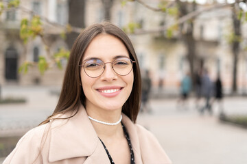 Portrait of a cheerful woman wearing glasses and smiling standing in the city park 