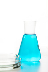 Laboratory chemical flask and petri dish with blue liquid on white background, for experiments.