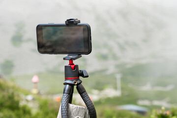 Smartphone on the tripod taking photos. Capturing image or time lapse of moving clouds in the mountains. Device for blogging 