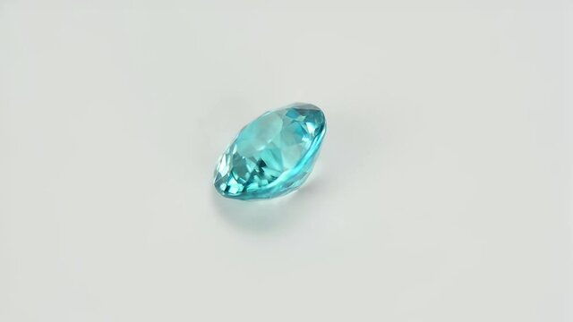 Natural rich electric blue oval bullet faceted in Thailand heated zircon clean gemstone in tweezers on daylight from window. Light gray gradient background.